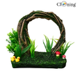 Decorative aquarium scene with a wooden arch, plants, and small figurines on a white background.