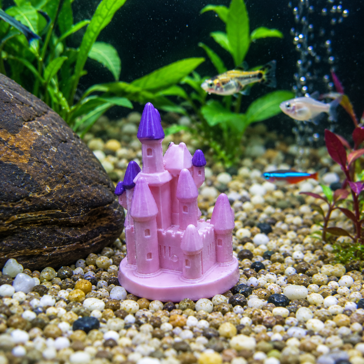 Pink castle ornament in an aquarium with gravel, rocks, and fish.